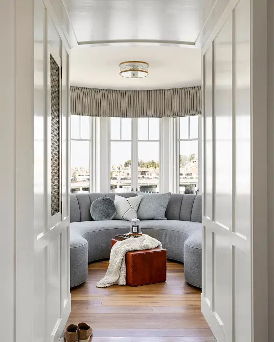 Lounge room with plush grey couch, windows on all sides, light wood flooring and natural light creating airy atmosphere