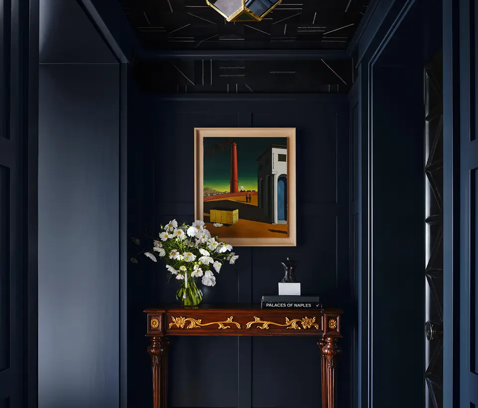 Elegant hallway with dark walls, framed artwork, and a wooden console table with flowers.