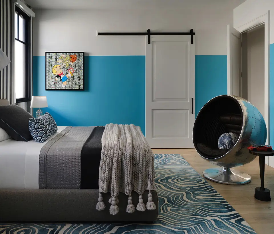 Modern bedroom with bold blue accents, patterned rug, cozy bedding, and a unique metallic pod chair.