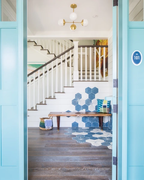 Entryway with open door, wide staircase, wooden bench and navy blue-gray hexagon floor tiles from lido house balboa cottage