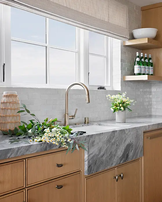 Park Ave kitchen with light gray marble counters, white wall tile, light brown cabinets, and windows.
