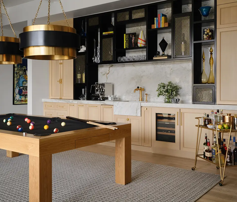 Modern game room with light wood cabinetry, marble backsplash, pool table, gold accents, and a stocked bar cart.