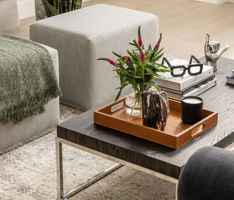 Modern living room coffee table styled with books, a leather tray, fresh flowers, a candle, and decorative accents.