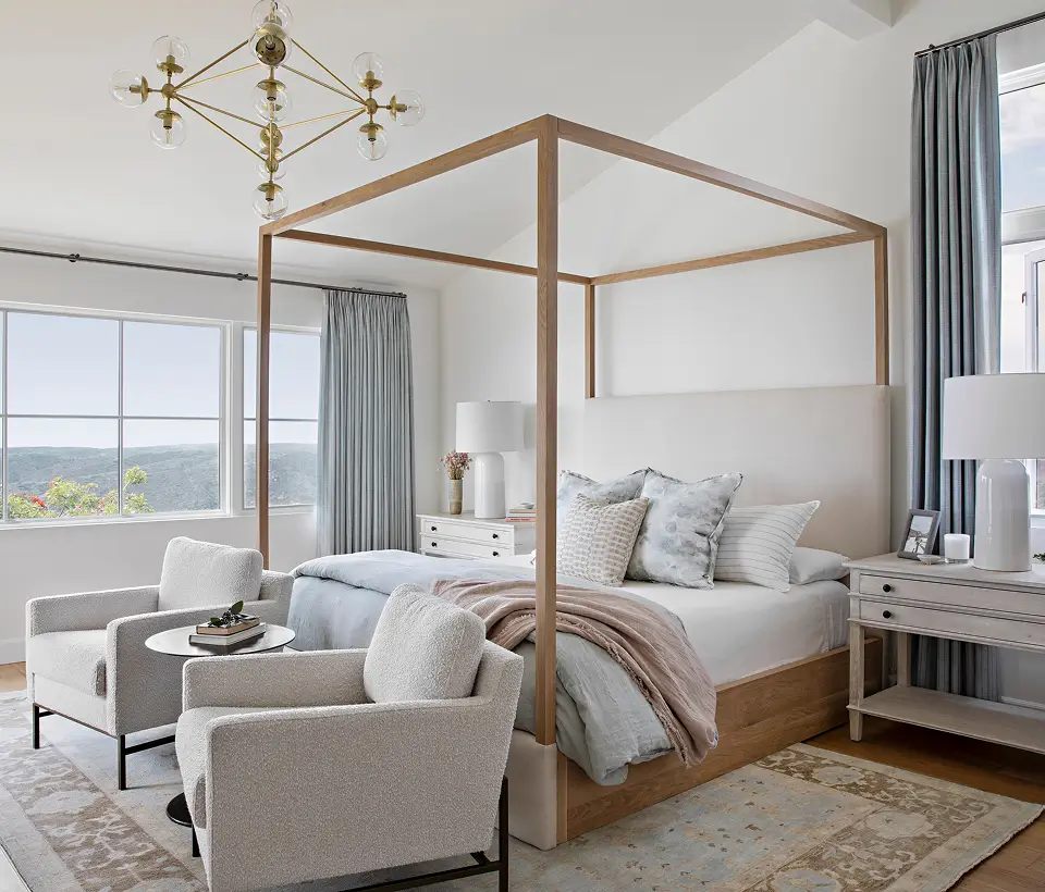 Elegant bedroom with canopy bed, soft neutral decor, two accent chairs, and large windows bringing in natural light and hillside views.