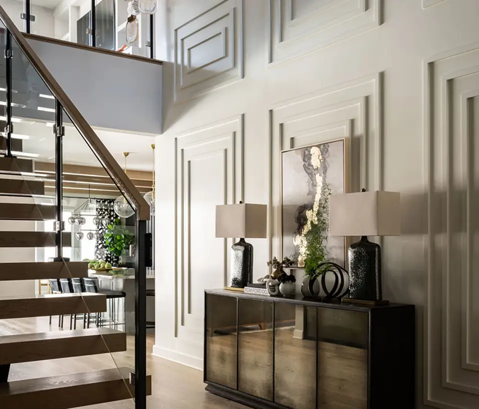 Grace Blu’s Trailmaster interior design with wood staircase, white vertical paneling, and decorative console table styling with two lamps.