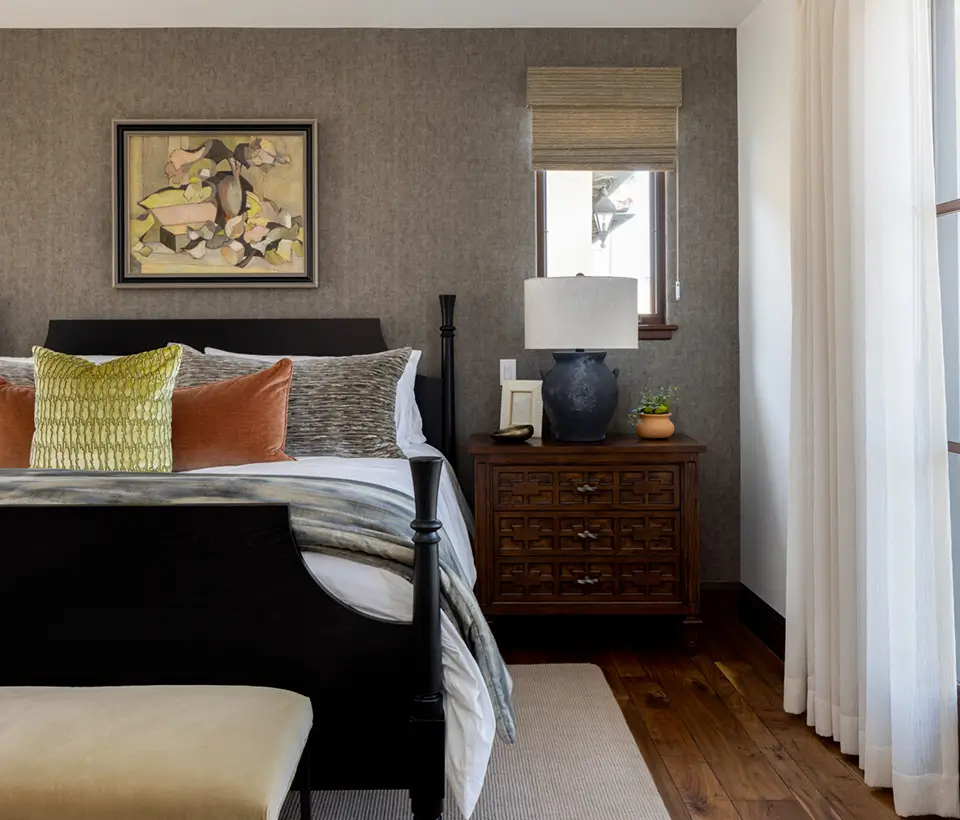 Bedroom with dark wood bed frame, textured pillows, wooden nightstand, table lamp, and wall art above the bed.