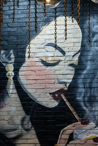 painting of a woman smoking a cigarette on a brick wall in a restaurant