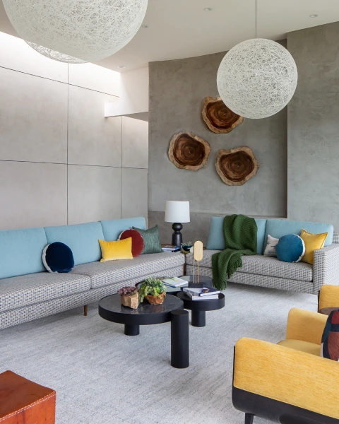 Light gray living room with colorful cushions, wood wall art, and white pendant lights above by Grace Blu.