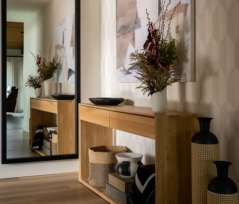 Modern entryway with wooden console table, decorative vases, abstract wall art, and large mirror reflecting the hallway.