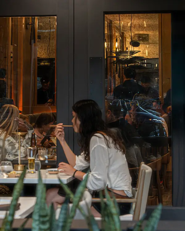 Guests enjoying dinner at Yuzu Sushi, seen through glass windows with a warm, lively ambiance inside.