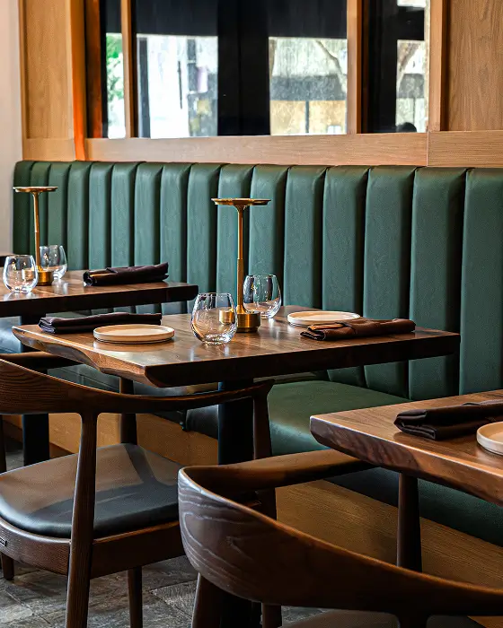 Modern restaurant interior with green booth seating, wooden tables, and neatly set glassware.