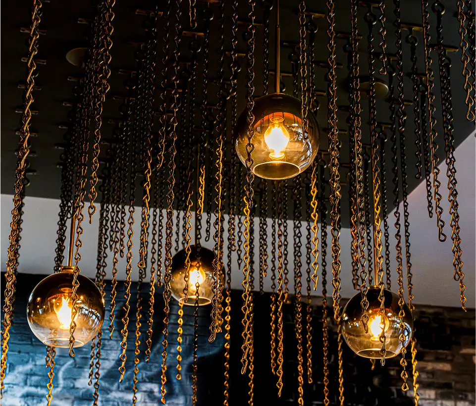 Warm glass pendant lights suspended on gold chains from a dark ceiling, creating a moody, modern ambiance at Yuzu Sushi.