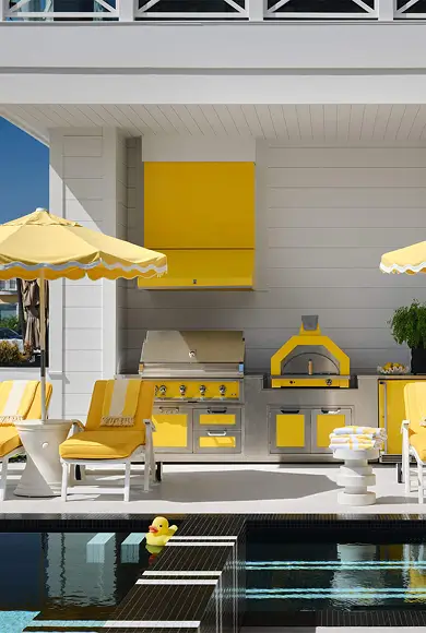 Vibrant poolside outdoor kitchen with yellow accents, lounge chairs, umbrellas, and a playful rubber duck in the water.