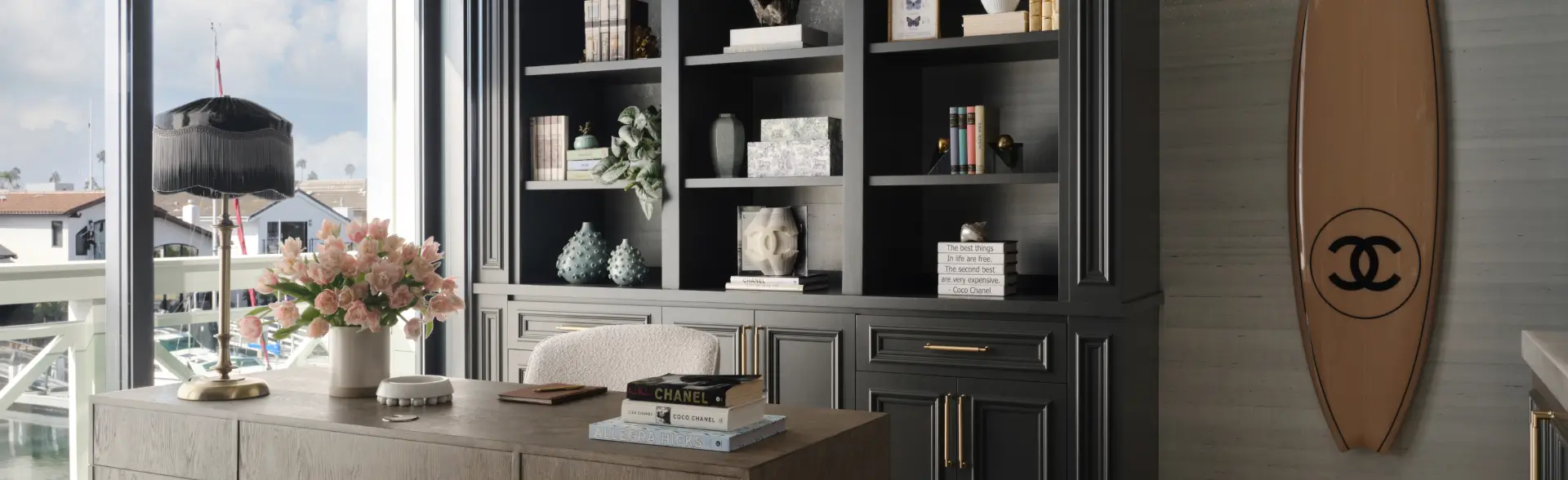 Chic home office with black built-ins, Chanel surfboard, marina view, and curated decor styled by Grace Blu Design.