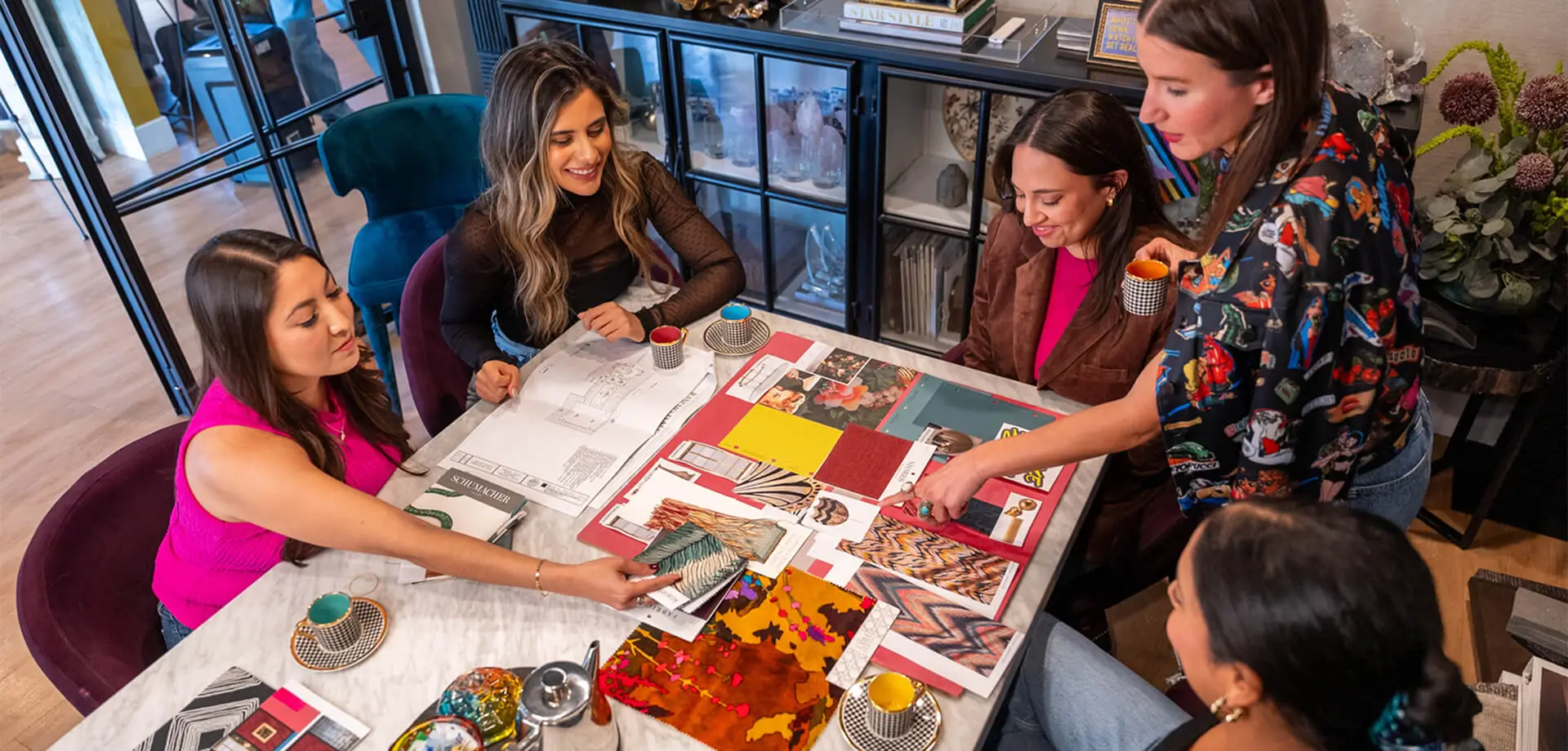 Interior design team reviewing material swatches and laughing together at a colorful workspace with floral artwork in the background