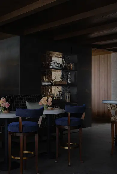 Moody luxury lounge with velvet chairs, leopard barstools, dark wood paneling, and custom built-in bar shelving.