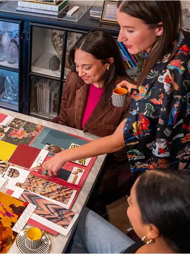 Interior design team reviewing material swatches and laughing together at a colorful workspace with floral artwork in the background