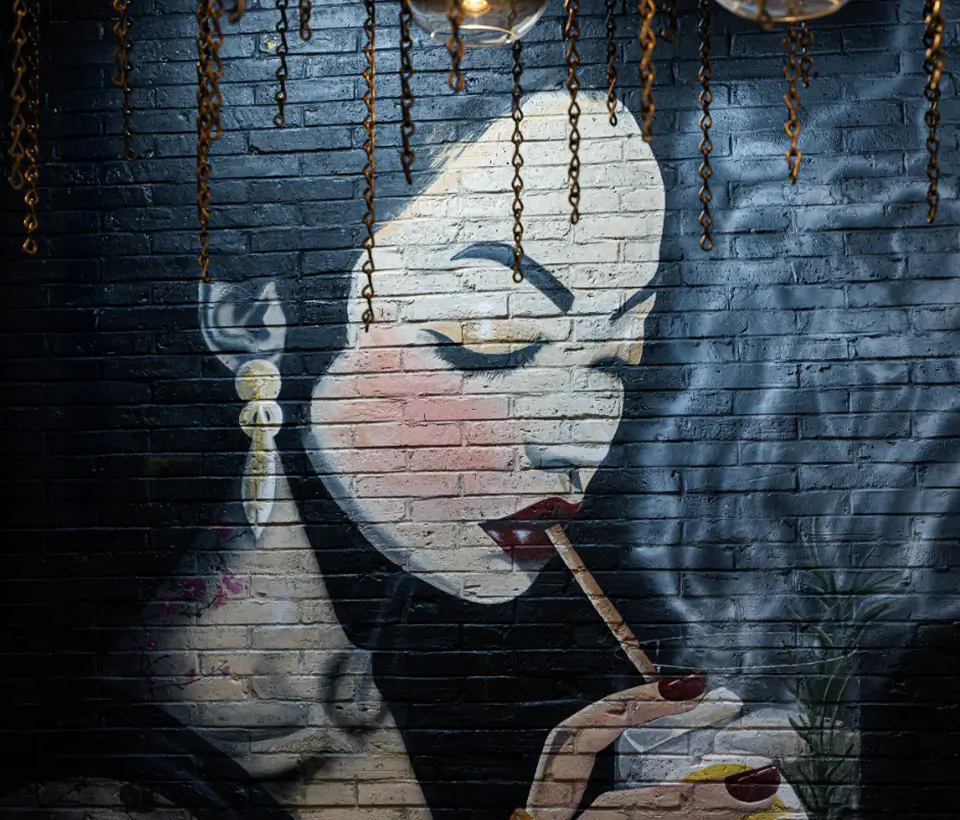 Mural at Yuzu Sushi of an elegant woman with bold makeup smoking beside a drink.