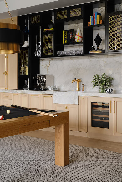 Luxury home bar with marble backsplash, custom wood cabinetry, gold accents, and a modern black pool table.