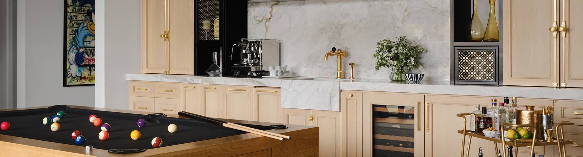 Luxury home bar with marble backsplash, custom wood cabinetry, gold accents, and a modern black pool table.