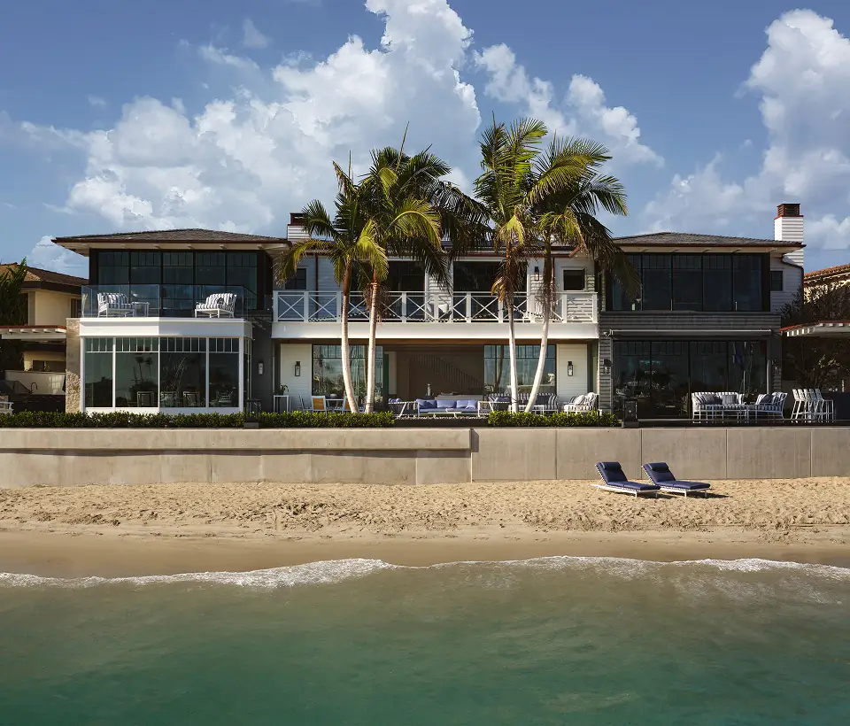 Modern beachfront home with palm trees, ocean-facing balconies, and coastal outdoor lounge areas designed by Grace Blu.