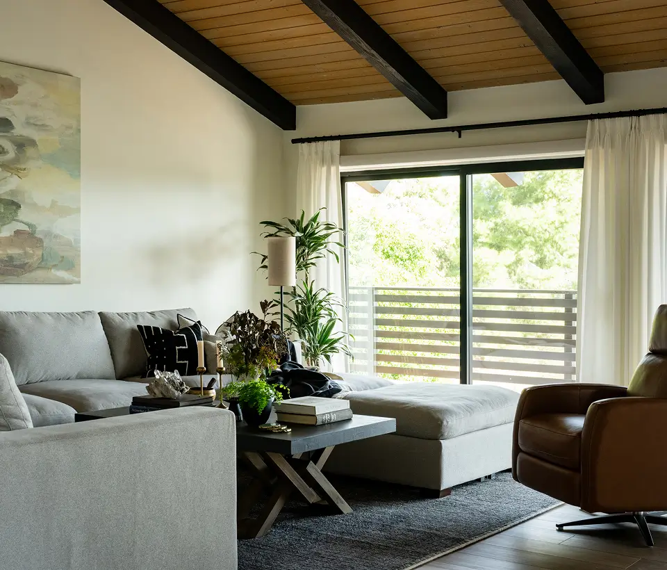 Cozy living room with gray sectional sofa, modern coffee table, indoor plants, and large sliding glass door with natural light.