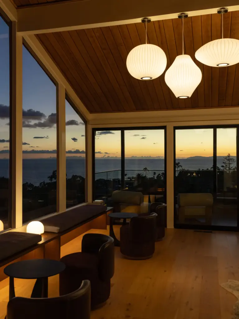 Living room at dusk with lit bubble pendants and a sunset ocean view