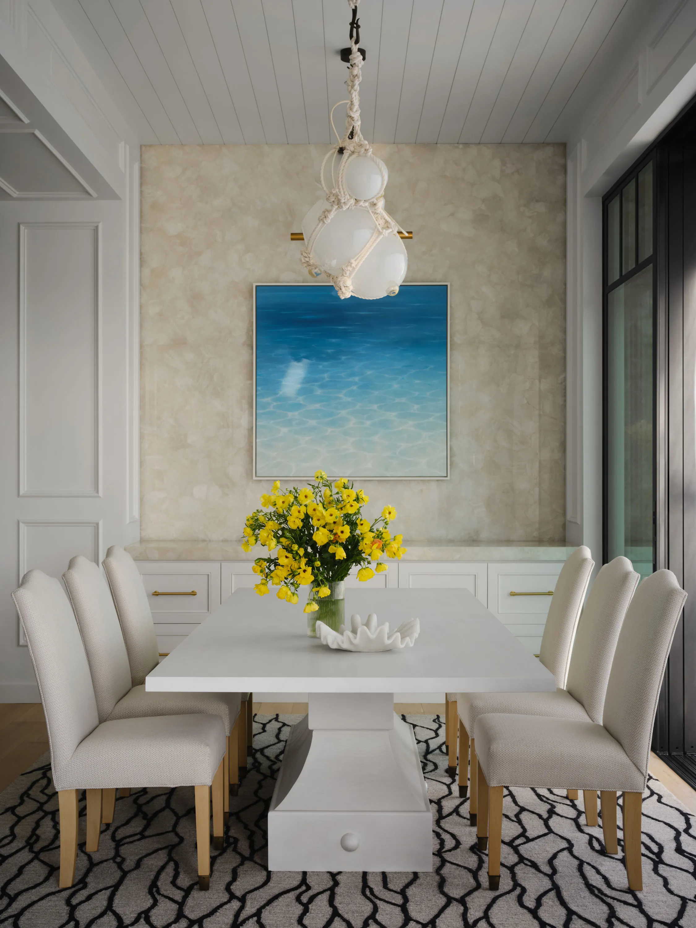 Dining room with a white pedestal table, ocean painting and shell chandelier